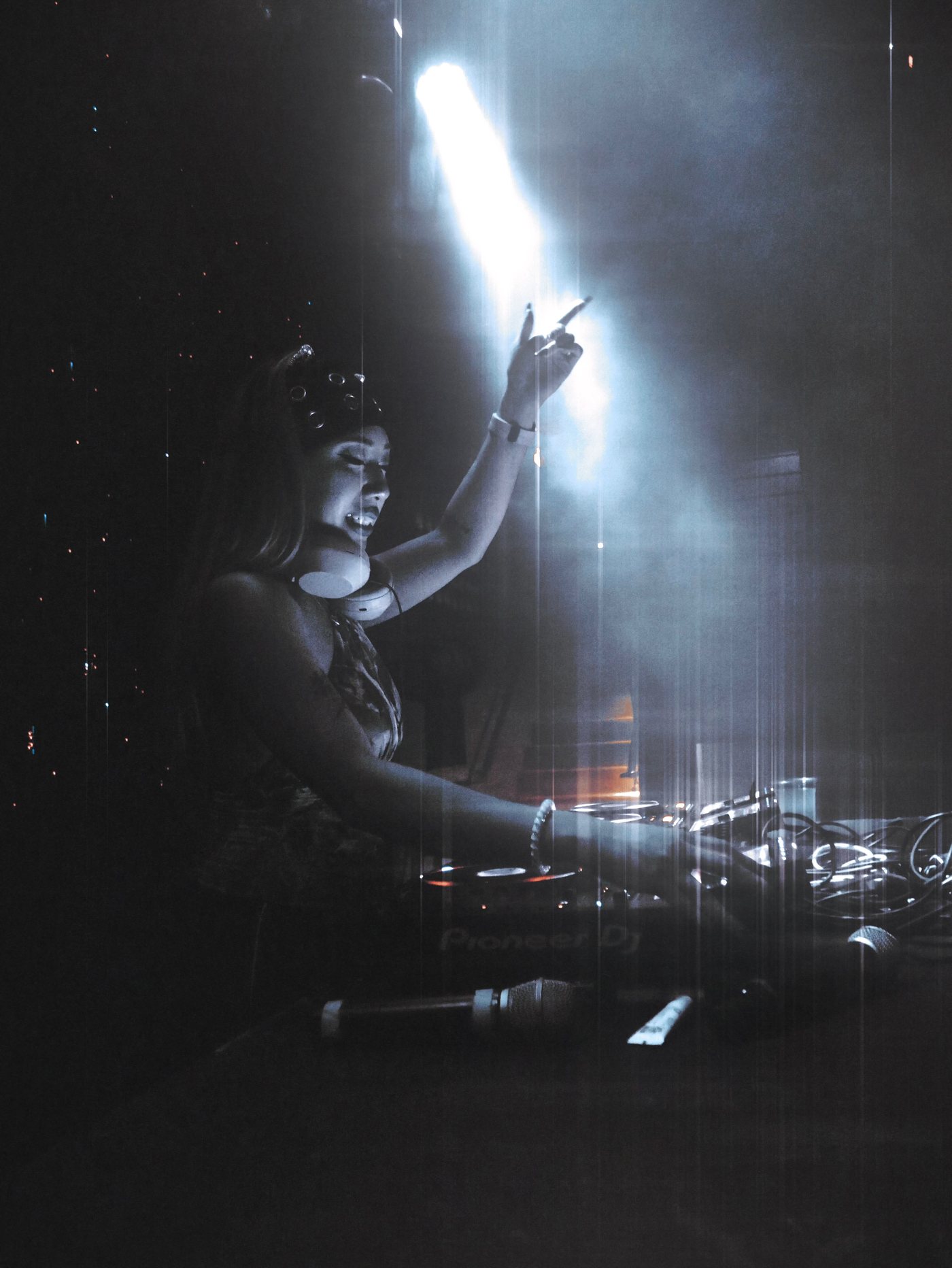 Seduza behind the decks, arm raised in a single spotlight, cat ears silhouetted